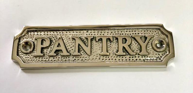 Może przedstawiać: Srebrny metalowy znak z wytłoczonym napisem "PANTRY". Znak ma po dwa otwory po obu stronach do zawieszenia.