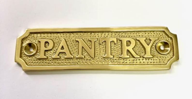 Może przedstawiać: Mosiężny znak z wytłoczonym napisem "PANTRY". Znak ma ozdobną ramkę i dwa małe otwory po obu stronach.