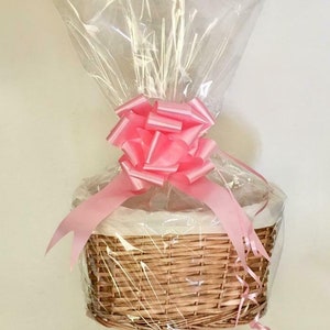 May include: A wicker basket wrapped in clear cellophane with a pink bow and pink ribbon.