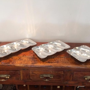May include: Three silver serving trays with wavy edges and four compartments. The trays are arranged on a wooden table.