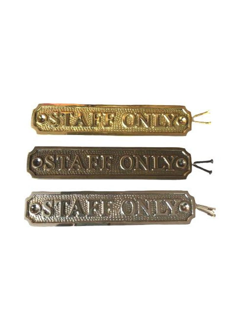 May include: Three rectangular metal signs with a textured background and the embossed text "STAFF ONLY" in capital letters. Each sign features a screw hole on both ends and includes two small mounting screws attached to the right side.