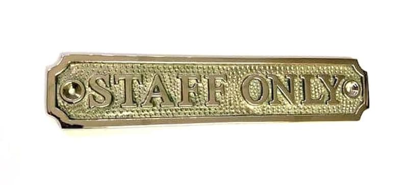 May include: A rectangular brass sign with a textured background and polished edges. The sign features the embossed text "STAFF ONLY" in capital letters. There are two circular screw holes, one on each end of the sign for mounting purposes.