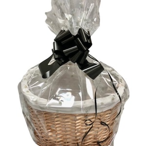 May include: A wicker basket with a white liner and a black bow. The basket is wrapped in clear cellophane with white polka dots.