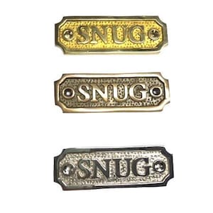 SNUG door sign made from solid brass with a choice of finish. Brass, nickel or antique bronze. The plaque comes with screws, 9.8x3.3x0.4cm.