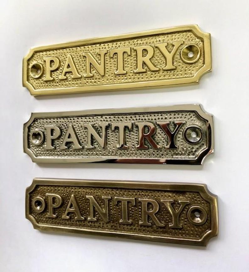 Może przedstawiać: Trzy mosiężne tabliczki na drzwi z wytłoczonym napisem "PANTRY". Tabliczki są w r&oacute;żnych wykończeniach: polerowane mosiądz, satynowy mosiądz i antyczny mosiądz.