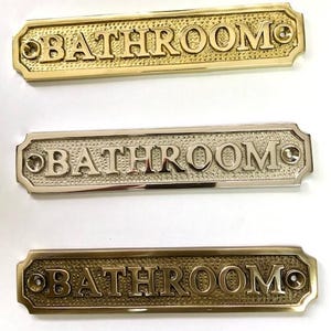 Letrero para puerta de baño disponible en tres acabados: níquel, bronce antiguo o latón. Incluye tornillos a juego. 16,2 cm x 3,3 cm.