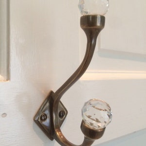 May include: A brass coat hook with two crystal knobs. The hook is curved and has a square base.