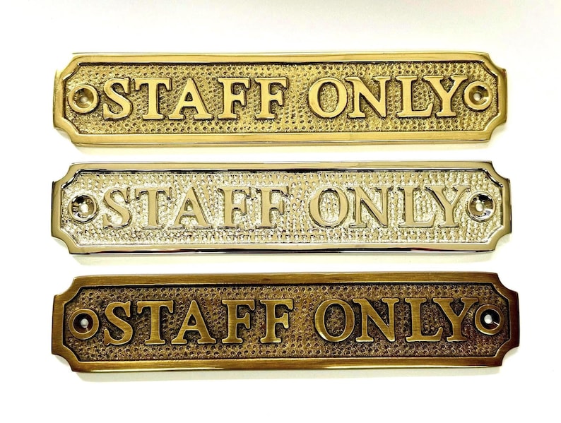 May include: Three rectangular metal signs with rounded corners, each featuring the embossed text "STAFF ONLY" in capital letters. The signs have a textured background and two screw holes on the ends, presented in brass, polished chrome, and antique bronze finishes.