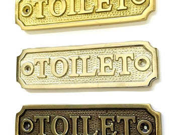 May include: Three rectangular toilet signs in gold, brass, and bronze tones. Each sign has the word "TOILET" in capital letters. The signs have a textured background and are designed with screw holes for mounting.