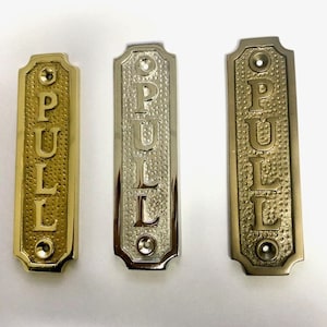 Peut inclure: Trois plaques de porte en métal, une dorée, une argentée et une en laiton. Chaque plaque porte l'inscription "PULL" en caractères décoratifs.