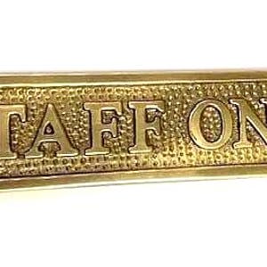 May include: A rectangular brass sign with a textured background and raised lettering that reads STAFF ONLY. The sign features a polished border and two circular mounting holes, one on each end, designed for attachment to a door or wall surface.