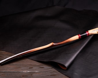 May include: A wooden bow with a black and red wrap and a bone handle. The bow is resting on a black leather surface.