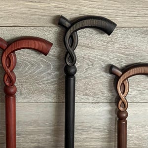 Peut inclure: Trois cannes de marche en bois avec des motifs de nœuds complexes. Les cannes sont teintées dans des tons de rouge, brun et noir.