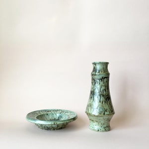May include: A green glazed ceramic vase and a matching green glazed ceramic bowl. The vase has a flared top and a rounded bottom. The bowl has a wide rim and a shallow well.