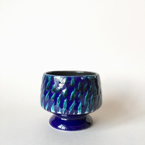May include: A blue and green ceramic planter with a geometric pattern. The planter has a wide base and a narrow top.