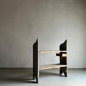 May include: A two-tiered wooden shelf unit with a gray painted finish. The shelf has a simple design with two shelves and four legs. The shelf is made of wood and has a rustic look.