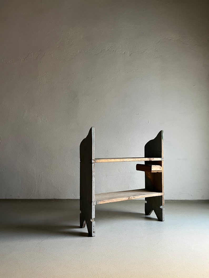 May include: A two-tiered wooden shelf unit with a gray painted finish. The shelf has a simple design with two shelves and four legs. The shelf is made of wood and has a rustic look.