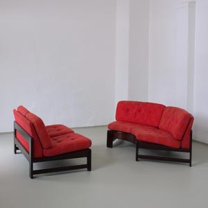 May include: A set of two red modular sofas with dark wood frames. The sofas are arranged in a curved shape, creating a cosy seating area.