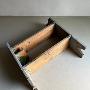 May include: A wooden stool with a gray and green paint finish. The stool has a simple design with two horizontal supports and a rectangular base.