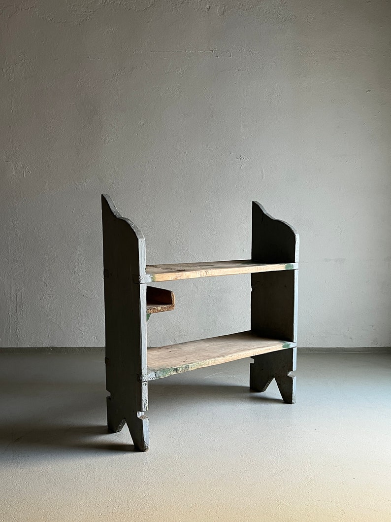 May include: A two-shelf wooden shelving unit with a gray painted finish. The shelves are made of natural wood and the unit has a simple, rustic design.