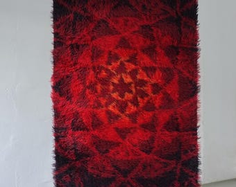 May include: A rectangular, shaggy rug with a vibrant color gradient. The rug transitions from deep black at the top to a fiery red and orange center, creating a striking visual effect. The texture appears plush and dense, suggesting a soft, comfortable feel.