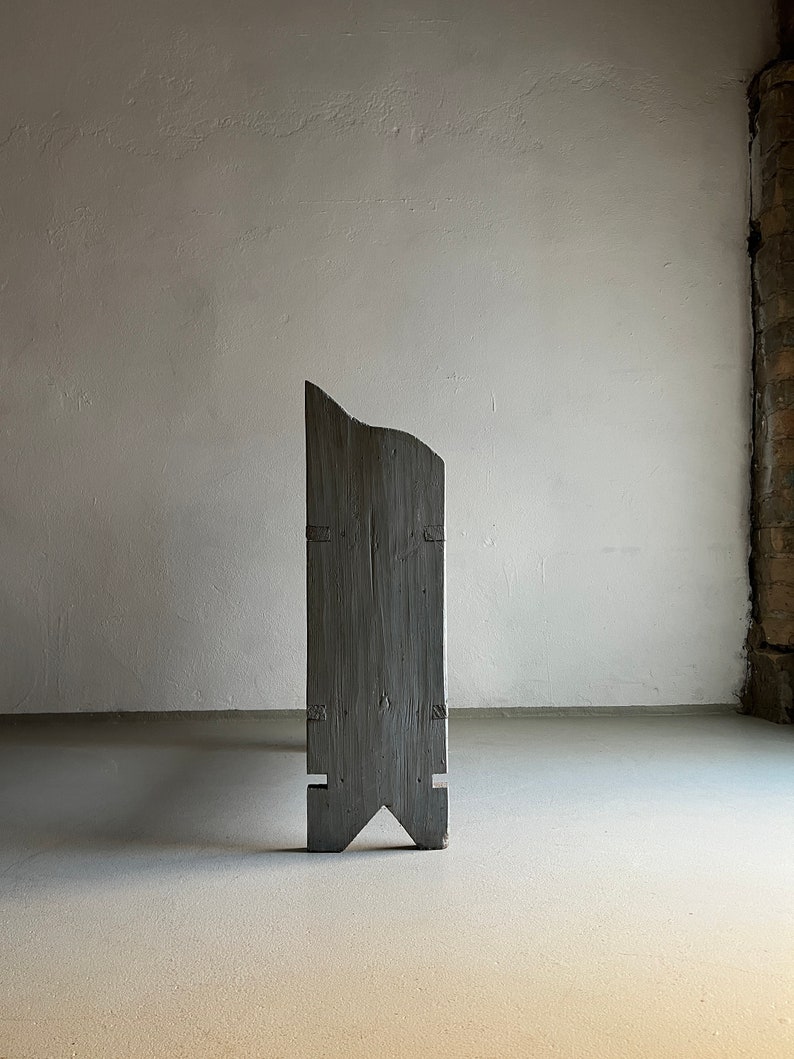 May include: A tall, gray wooden sculpture with a unique, asymmetrical shape. The sculpture has a pointed top and a wide base with two angled legs.