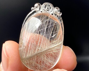 May include: A clear quartz pendant with a silver rutilated inclusion. The pendant is oval shaped and has a decorative bail.