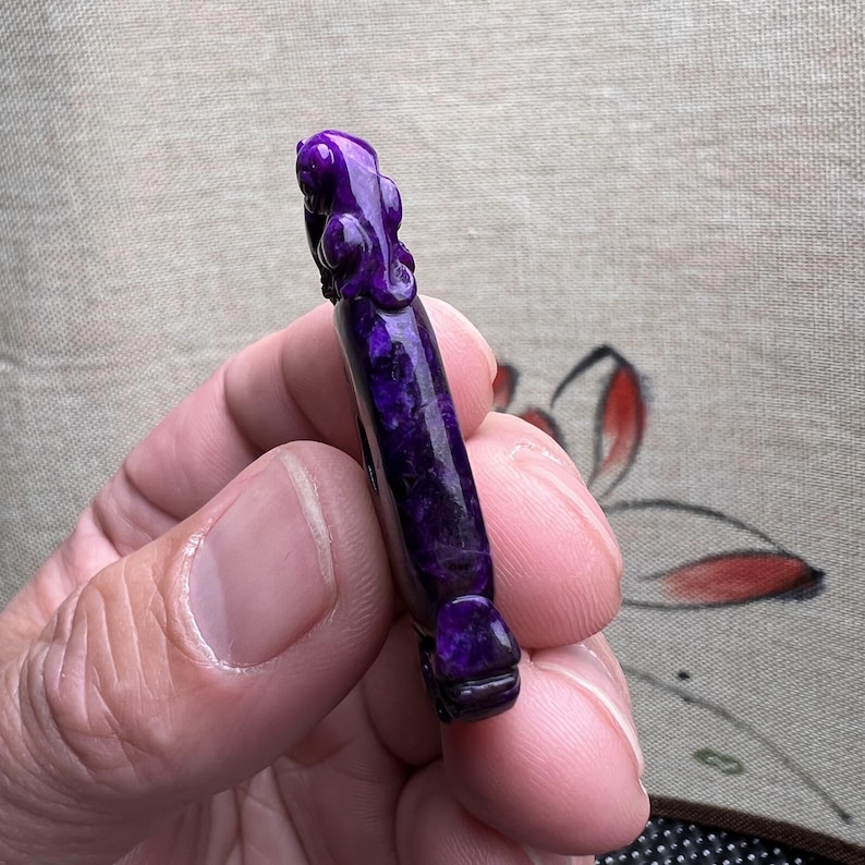 May include: A purple carved pendant with a detailed design. The pendant is made of a natural stone with a unique pattern.