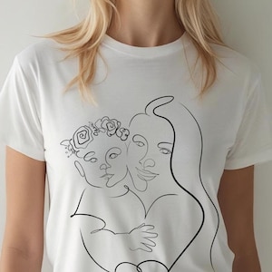 May include: White t-shirt featuring a black line art illustration of a mother and child. The child wears a floral crown. The design depicts the figures embracing, with the mother's hair flowing down.