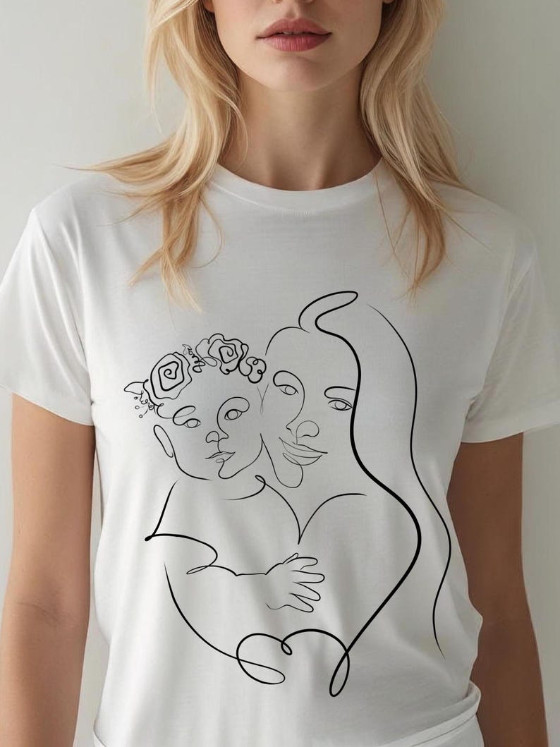 May include: White t-shirt featuring a black line art illustration of a mother and child. The child wears a floral crown. The design depicts the figures embracing, with the mother's hair flowing down.