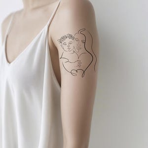 May include: A black line art tattoo of a mother and child embracing. The child wears a floral crown. The tattoo is on a person's arm, against a white background.