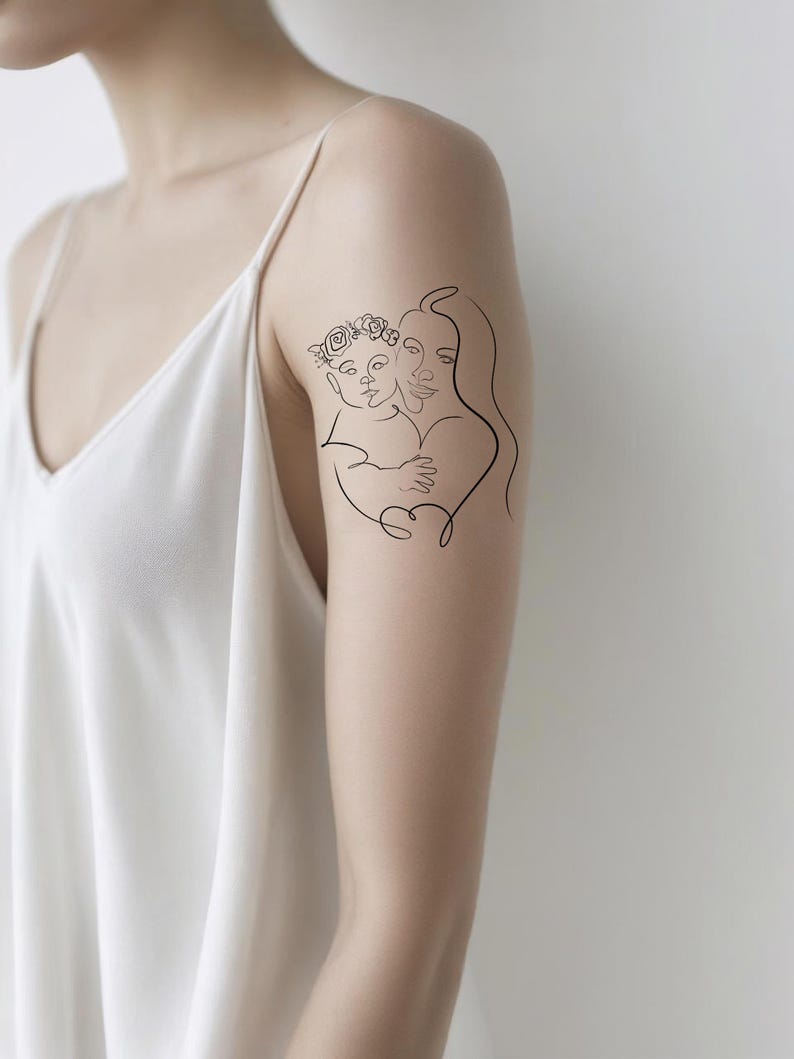 May include: A black line art tattoo of a mother and child embracing. The child wears a floral crown. The tattoo is on a person's arm, against a white background.