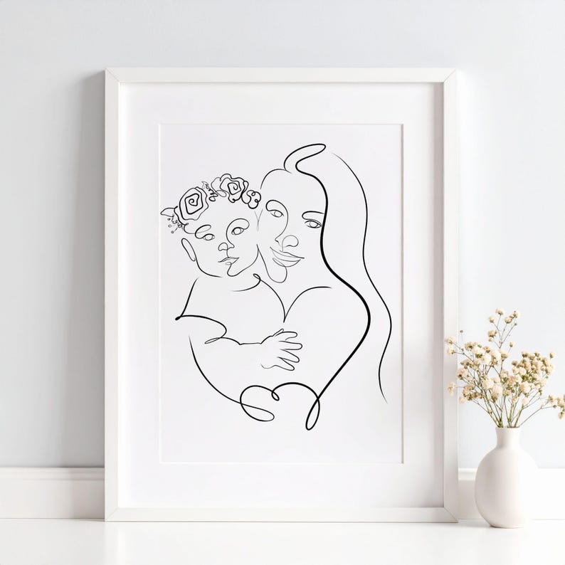 May include: A framed black and white line art print. The artwork depicts a mother holding a child, both faces are visible. The child wears a floral crown. The art is in a white frame, and a vase of flowers is in the background.