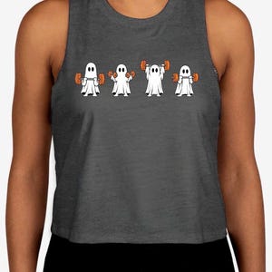 May include: A dark gray sleeveless crop top featuring a graphic print of four white ghosts in a row, each lifting orange dumbbells in different positions. The ghosts have simple black oval eyes and are depicted performing various weightlifting exercises.