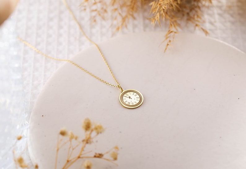 May include: A gold necklace with a round clock face pendant. The clock face has Roman numerals.