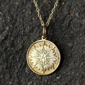 May include: A gold pendant necklace with a round charm featuring a stylized sun with a five-pointed star in the center.