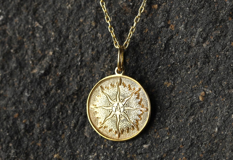 May include: A gold pendant necklace with a round charm featuring a stylized sun with a five-pointed star in the center.