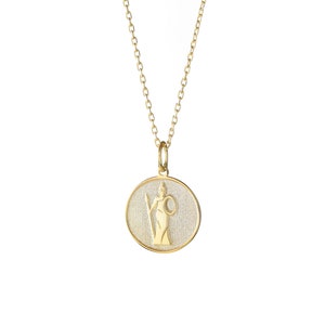 May include: Gold necklace with a round pendant featuring a detailed image of a woman holding a spear and a shield. The pendant has a textured surface.