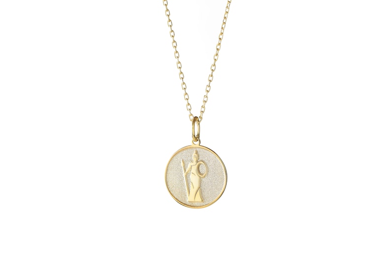 May include: Gold necklace with a round pendant featuring a detailed image of a woman holding a spear and a shield. The pendant has a textured surface.