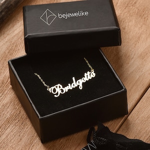 May include: A gold-colored necklace with the name "Bridgette" spelled out in cursive script. The necklace is in a black box with the word "bejewellike" printed on the top.
