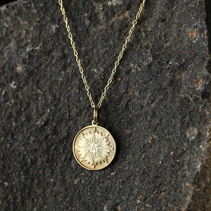 May include: A gold chain necklace with a round pendant featuring a stylized sun design.