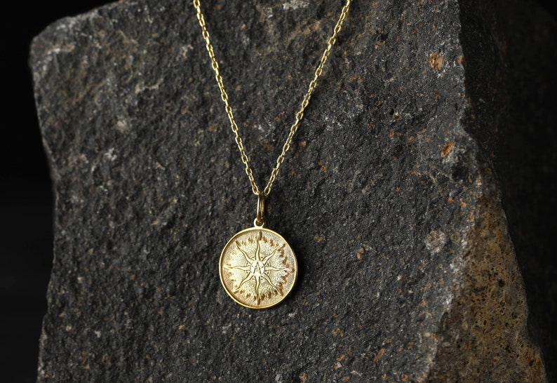 May include: A gold chain necklace with a round pendant featuring a stylized sun design.