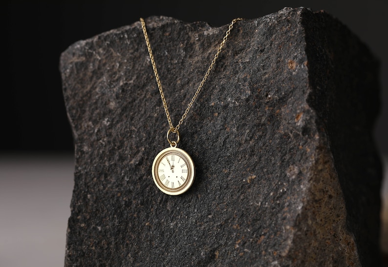 May include: A gold chain necklace with a round gold pendant featuring a white clock face with Roman numeral markings.