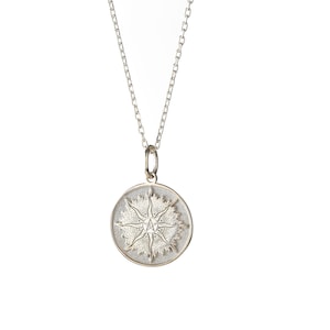 May include: A silver necklace with a round pendant featuring a detailed starburst design.