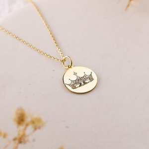 May include: A gold chain necklace with a round pendant featuring a crown design with small sparkling stones.