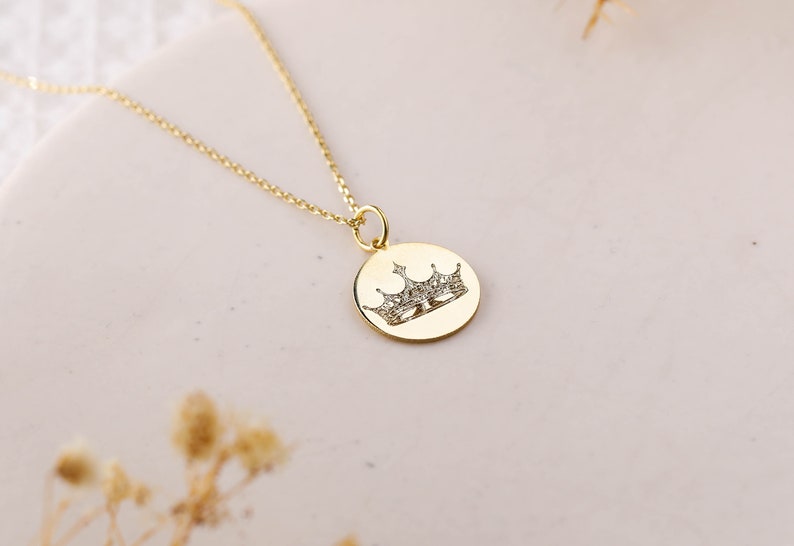 May include: A gold chain necklace with a round pendant featuring a crown design with small sparkling stones.
