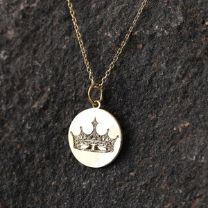 May include: A gold chain necklace with a round pendant featuring an engraved crown design.