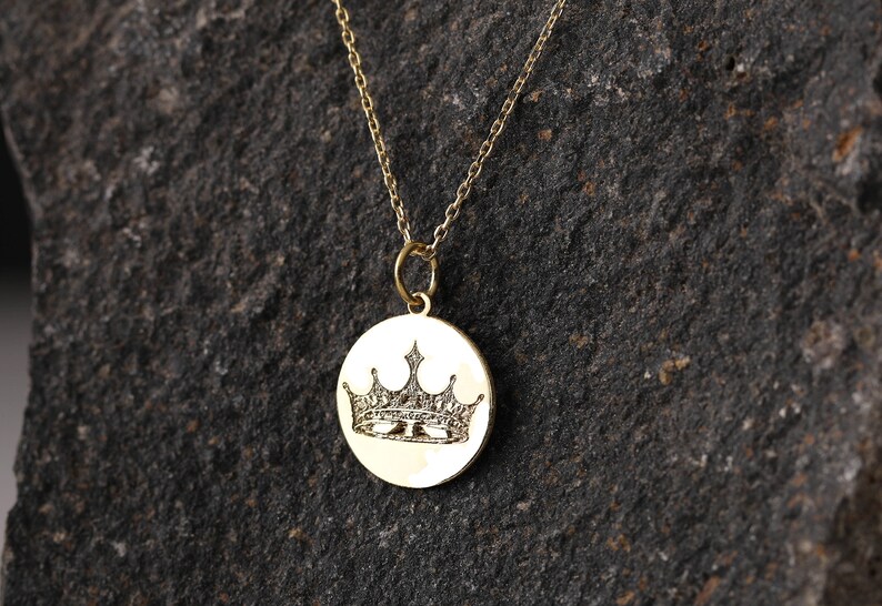 May include: A gold chain necklace with a round pendant featuring an engraved crown design.