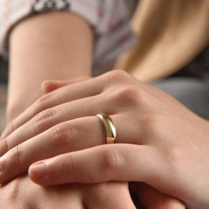 May include: A close-up of a person's hands with a gold wedding band on the ring finger.
