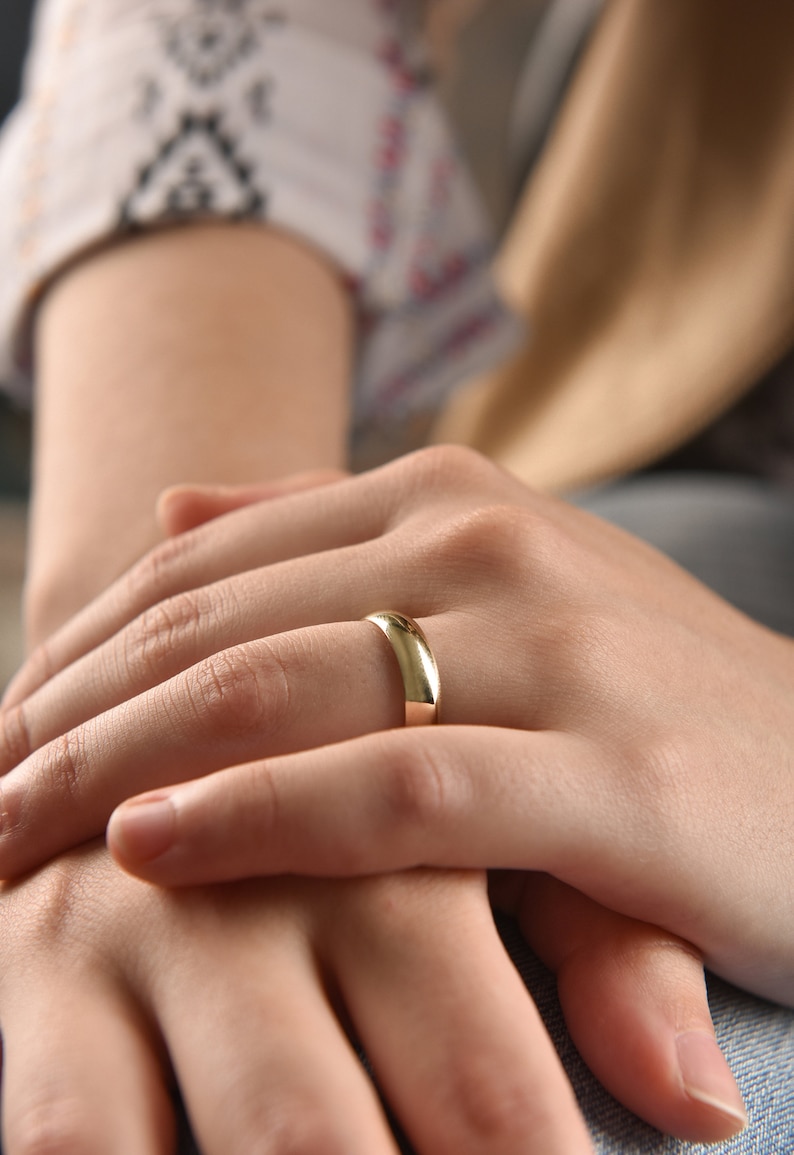 May include: A close-up of a person's hands with a gold wedding band on the ring finger.